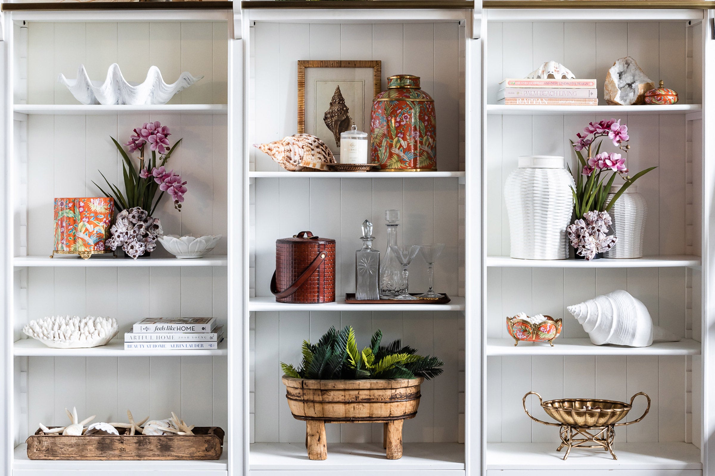 White Bookcase styled with coral, orange ceramics and orchids.