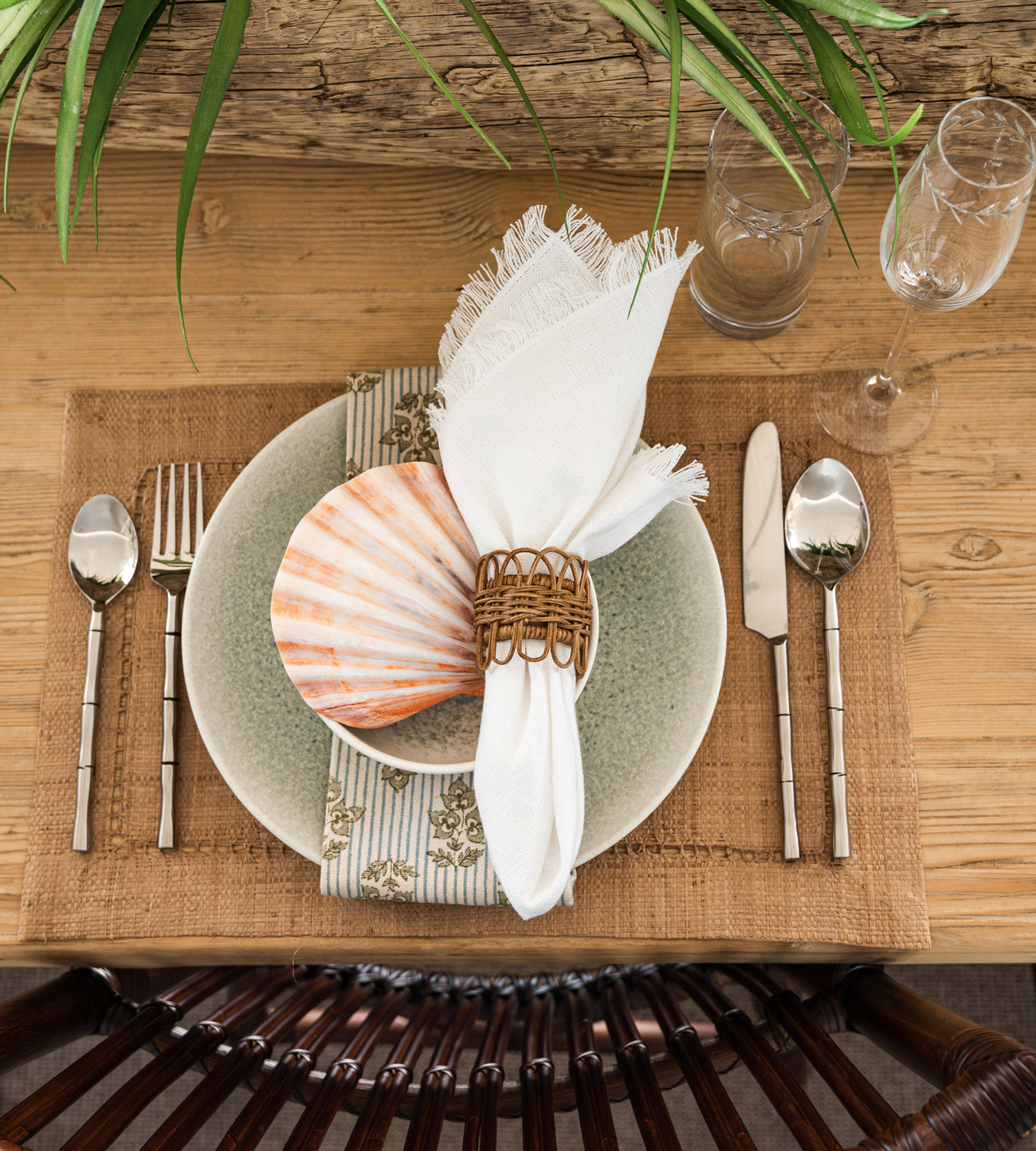 Fringed white napkin with rattan napkin ring on soft blue plates.