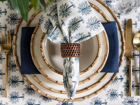 Palm print napery in blue and white with brown rattan napkin ring.