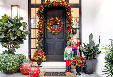 Decorative Christmas front door with wreath, nutcrackers, and potted plants.