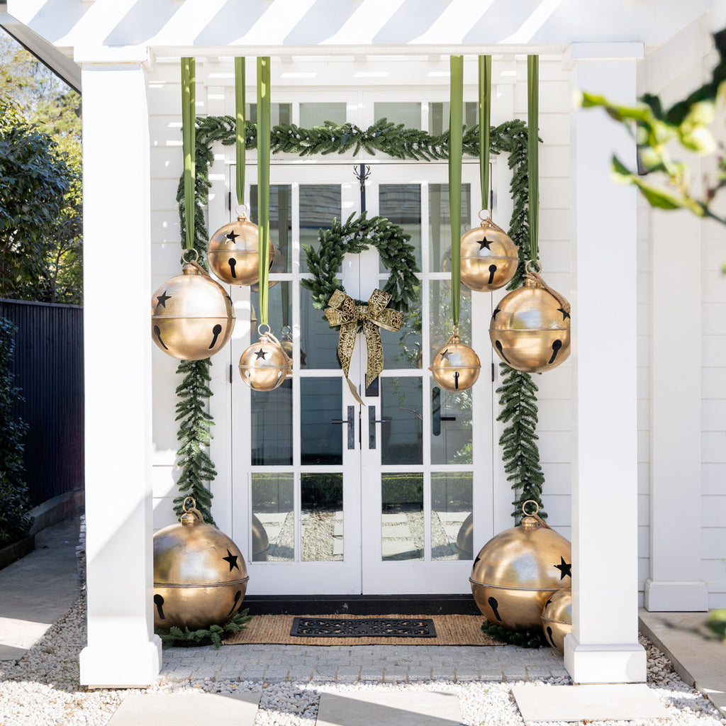 Decorative gold jingle bells hanging from green ribbon on a white door.