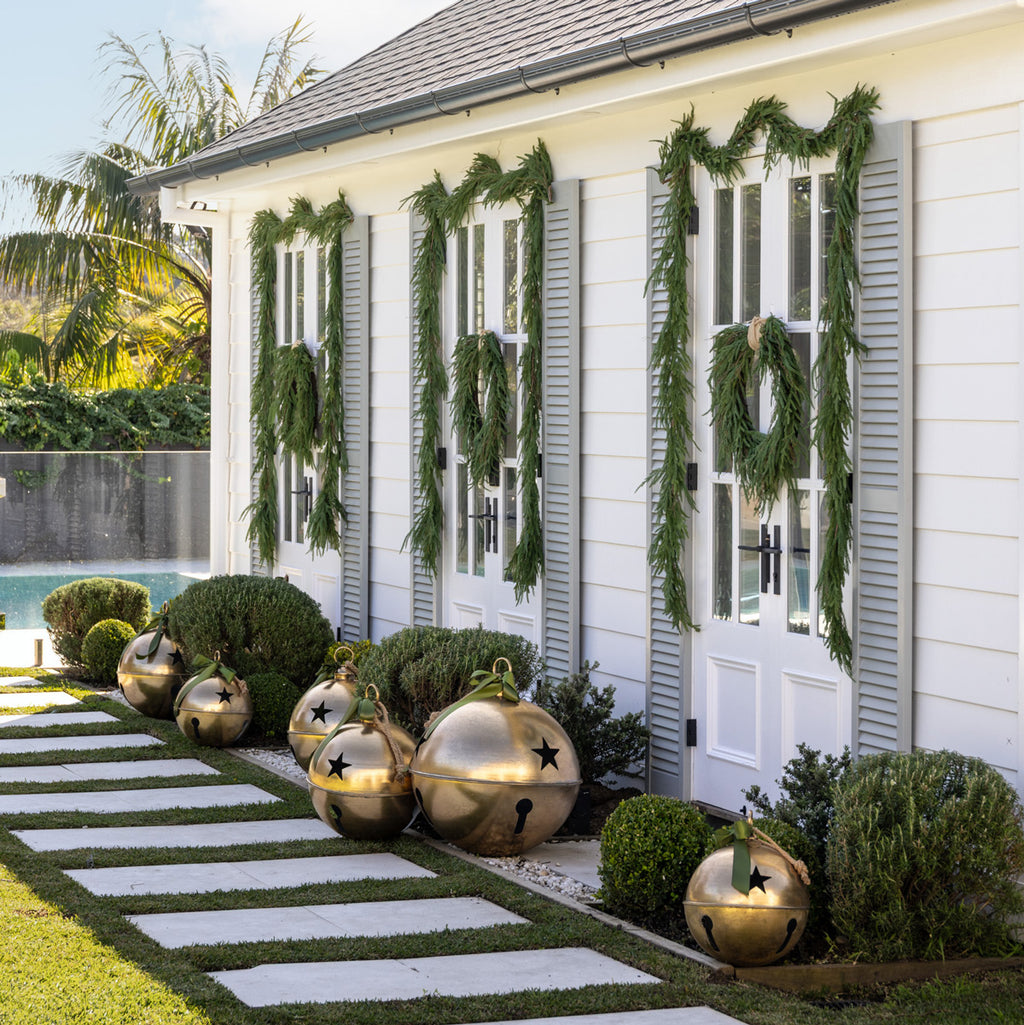 White poolhouse with Norfolk pine garland and wreaths with gold star bells.