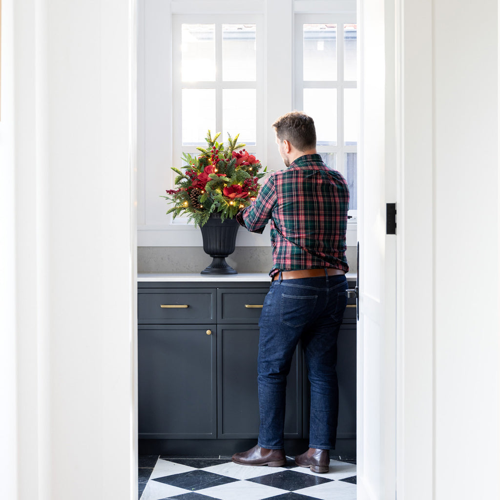 Man arranging flowers in a kitchen with a checkered floor and white walls.