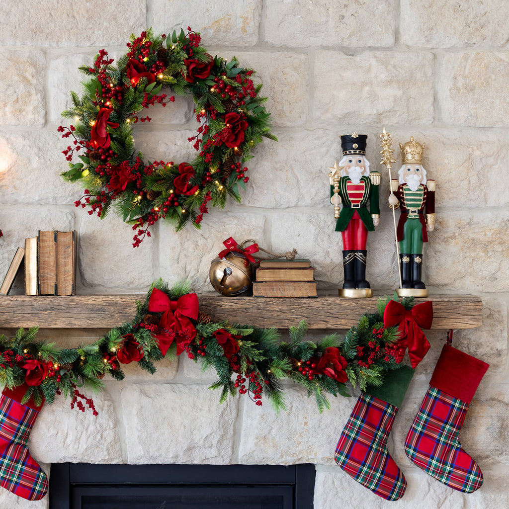 Decorative Christmas mantel with wreath, garland, nutcrackers, and stockings against a stone wall.