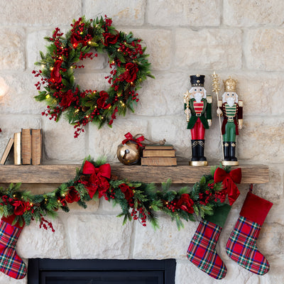 Decorative Christmas mantel with wreath, garland, nutcrackers, and stockings against a stone wall.