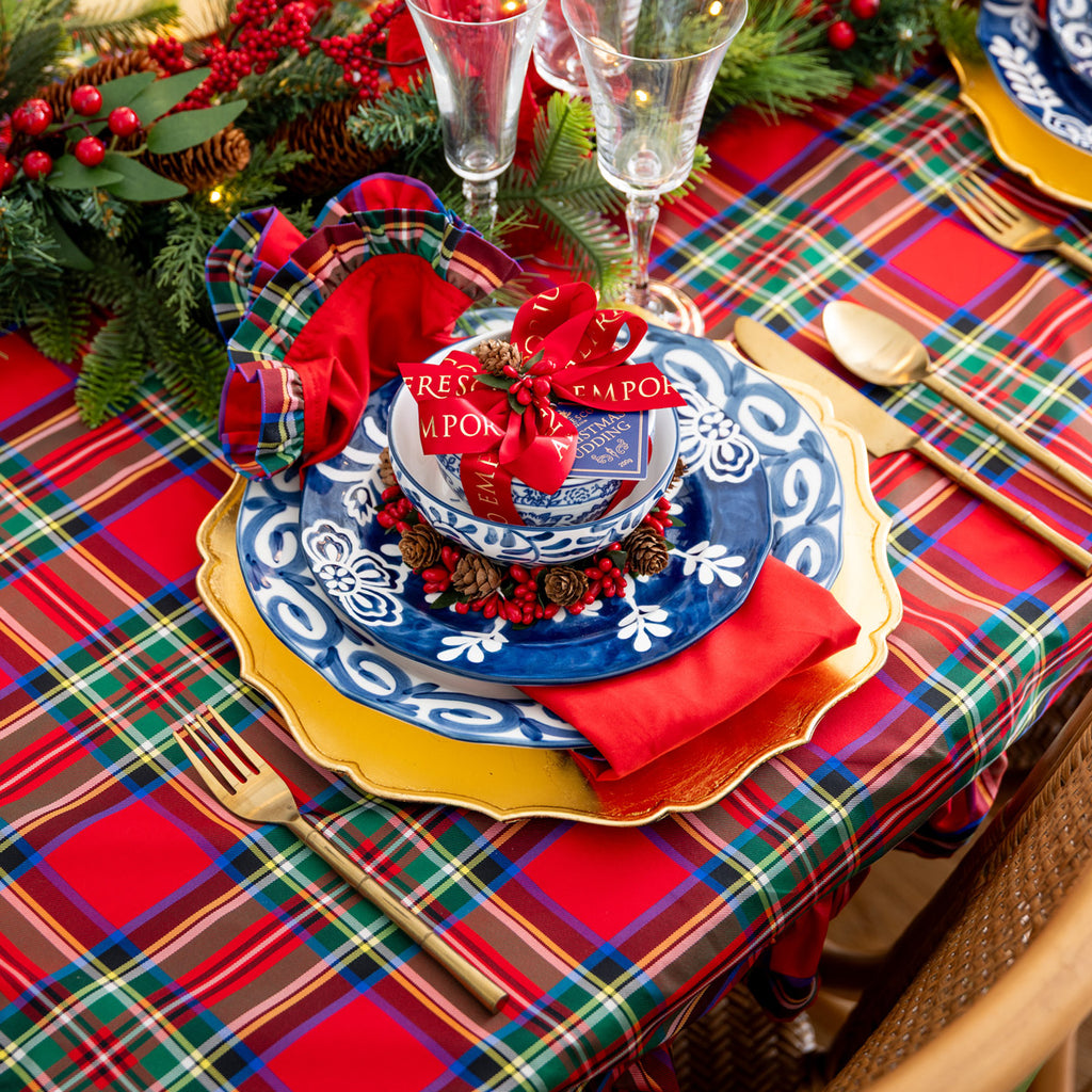 Christmas-themed table setting with plaid tablecloth, decorative plates, and red napkins.