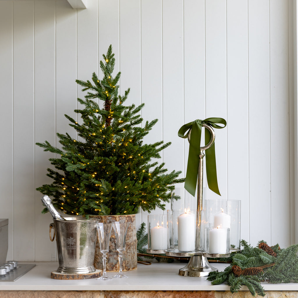 Decorative Christmas setup with a small tree, candles, and greenery on a white surface.
