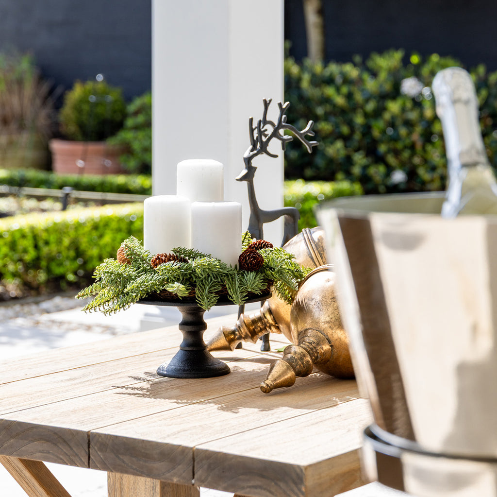 Decorative setup with candles, greenery, and deer figurines on a wooden table outdoors.