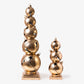 Two decorative gold ornaments stacked on wooden bases against a white background