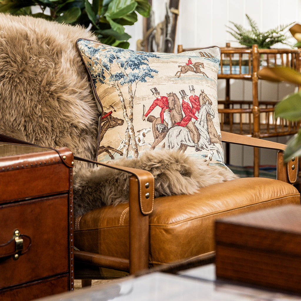 Brown leather armchair with decorative pillow featuring horse and rider design, surrounded by indoor plants.