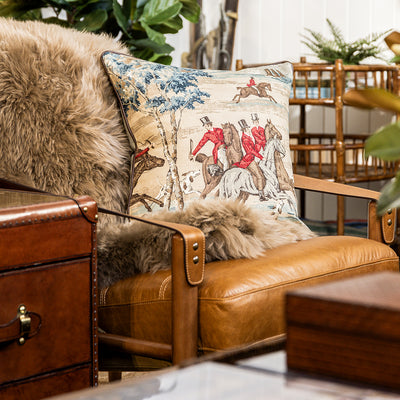Brown leather armchair with decorative pillow featuring horse and rider design, surrounded by indoor plants.