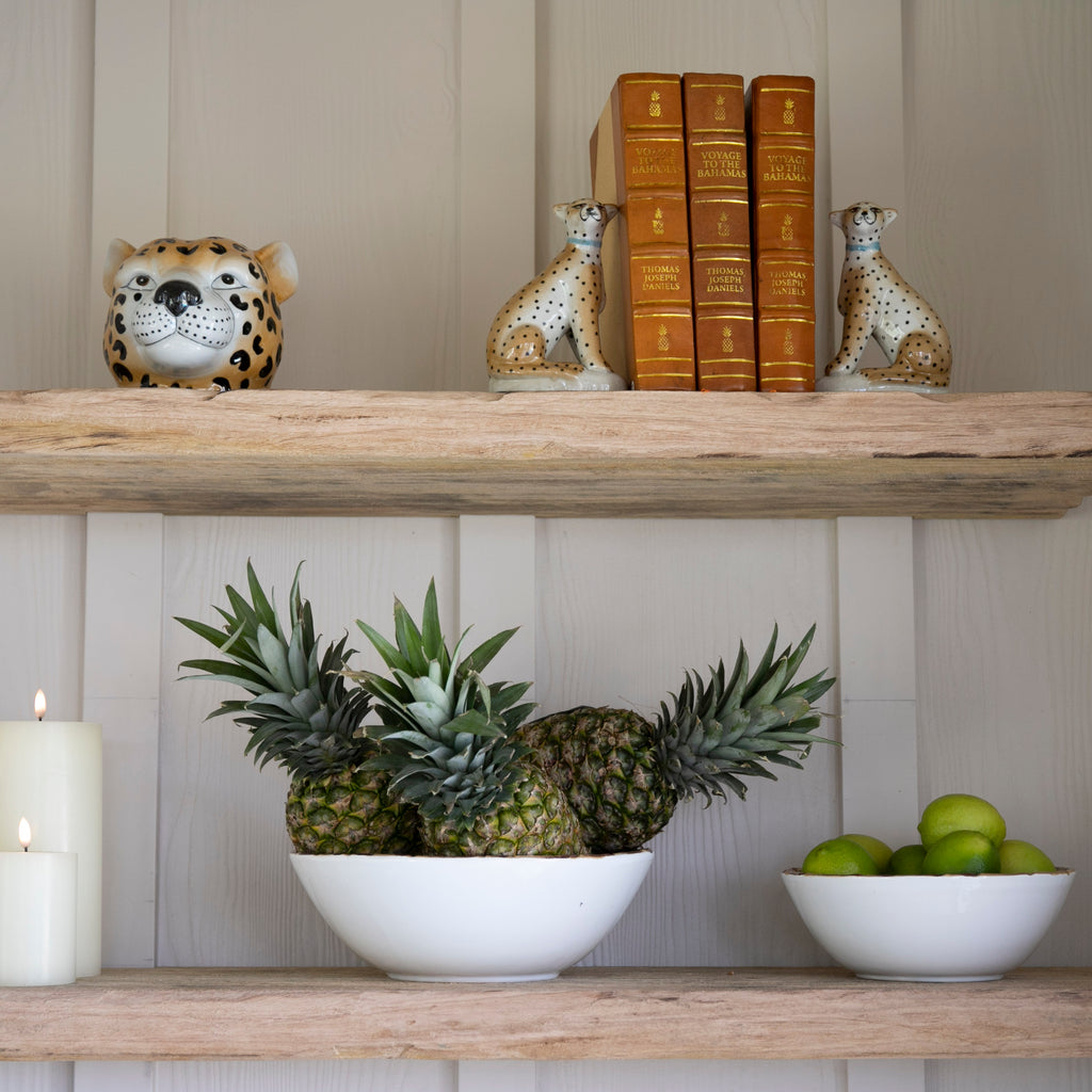 Large white bowl filled with pineapples on a shelf.