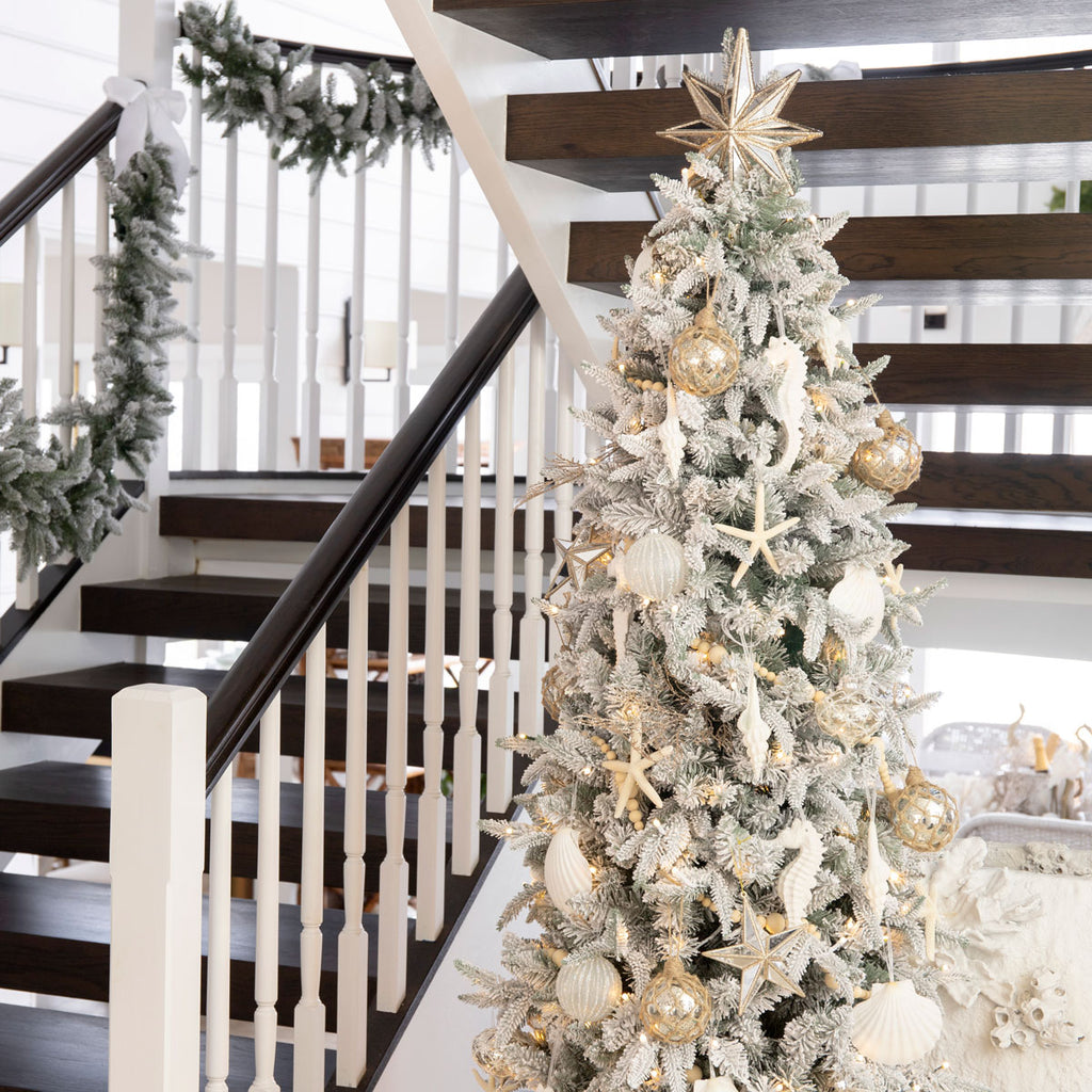 A decorated Slim Vermont Snowy Christmas Tree beside a staircase